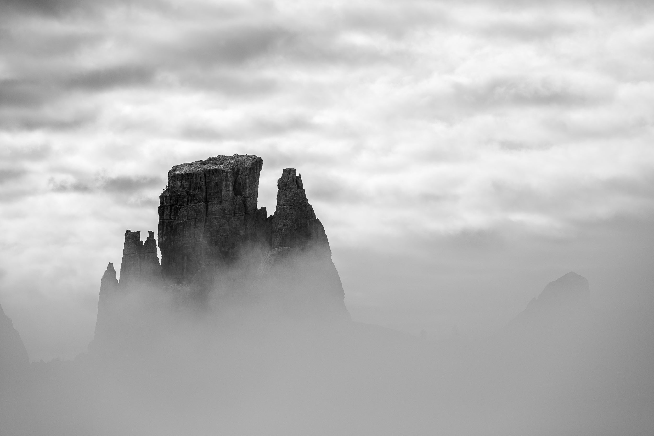 Stampa fine art in bianco delle Cinque Torri che emergono dalla nebbia in controluce