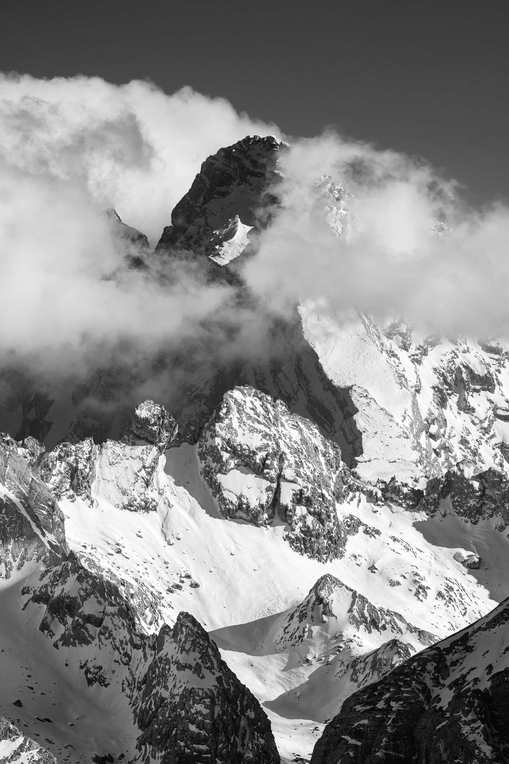 Fotografia in bianco e nero del Monte Antelao visto da un punto di ripresa insolito, con la vetta rocciosa che emerge tra le nuvole circondata da ampi nevai.